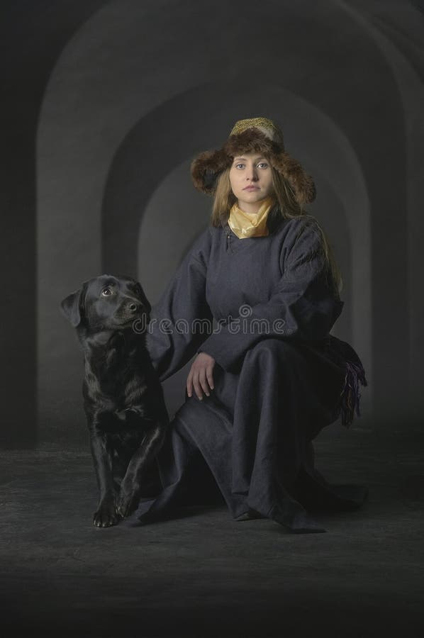 Young Woman in Traditional Fur Hat Kneeling with Black Dog in Dimly Lit Arched Corridor