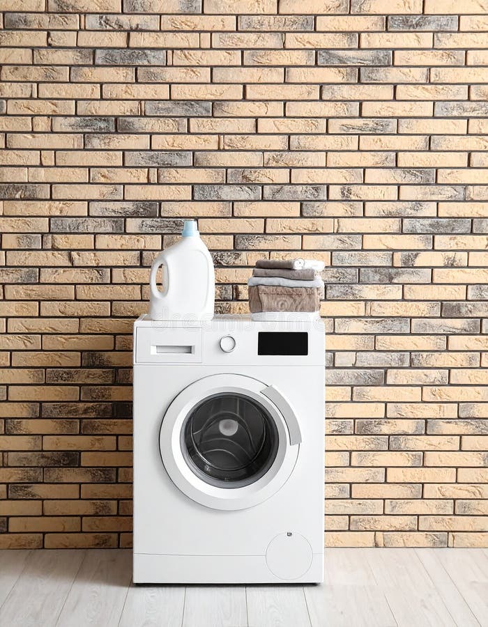 Front-loaded washing machine in a modern laundry room, set against a white brick wall. A potted plant and folded towels sit on top of the machine, adding a touch of greenery and organization. Next to it is a brown woven laundry basket. The area is tiled with neutral-colored flooring, and a striped rug lies in front of the appliances, providing a soft contrast to the sleek and clean design. Modern washing machine near brick wall in empty laundry room. Al Generated. Appliances front illustrations