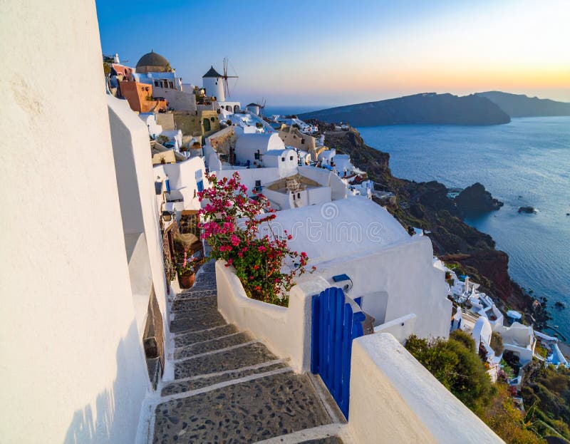 A picturesque view of Oia, Santorini, Greece, at sunset. Iconic white-washed buildings with vibrant blue doors and accents cling to the cliffside, overlooking the Aegean Sea. Stone steps lead down through the village, adorned with blooming pink bougainvillea. The warm hues of the sunset paint the sky, creating a serene and romantic atmosphere. This image captures the quintessential beauty of a Greek island paradise, perfect for travel and lifestyle themes. Sunrise stone steps illustrations