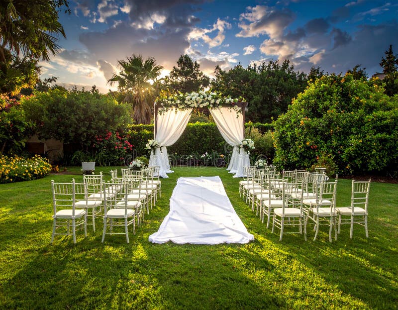 A beautifully arranged garden setting features two floral arches adorned with vibrant roses in shades of pink and white. Stone pathways lead to the arches, surrounded by lush greenery and meticulously trimmed hedges. The setup includes wooden chairs on either side of the path, suggesting a ceremonial or wedding arrangement. The backdrop includes various trees and colorful flowering plants under a partly cloudy sky, creating a serene and picturesque outdoor environment. Garden , Arch , Wedding. Al Generated. Wedding courtyard illustrations