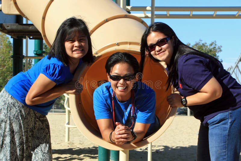 Three friends, a teenager and tw mature mid-30s females posing at a playground equipment with big smiles on their faces. A concept of friendship in separate generations. Three friends, a teenager and tw mature mid-30s females posing at a playground equipment with big smiles on their faces. A concept of friendship in separate generations.