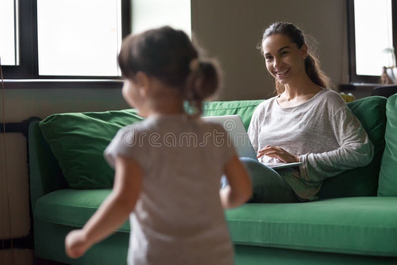 Generi lavorare al computer portatile mentre ragazza del bambino che gioca a casa fotografie stock Generi lavorare al computer portatile mentre ragazza del bambino che gioca a casa fotografie stock