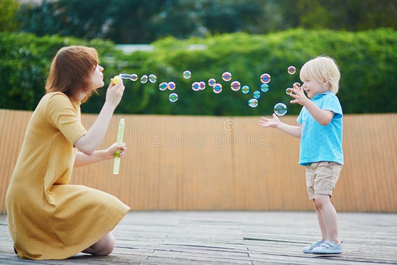Generi le bolle di salto ed il gioco con suo figlio piccolo immagine stock libera da diritti Generi le bolle di salto ed il gioco con suo figlio piccolo immagine stock libera da diritti