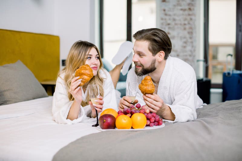 Genießen Sie das Frühstück, Obst, Croissants, Champagner Mann und Frau mit weißen Bademänteln beim Frühstück im Hotel lizenzfreie stockbilder Genießen Sie das Frühstück, Obst, Croissants, Champagner Mann und Frau mit weißen Bademänteln beim Frühstück im Hotel lizenzfreie stockbilder
