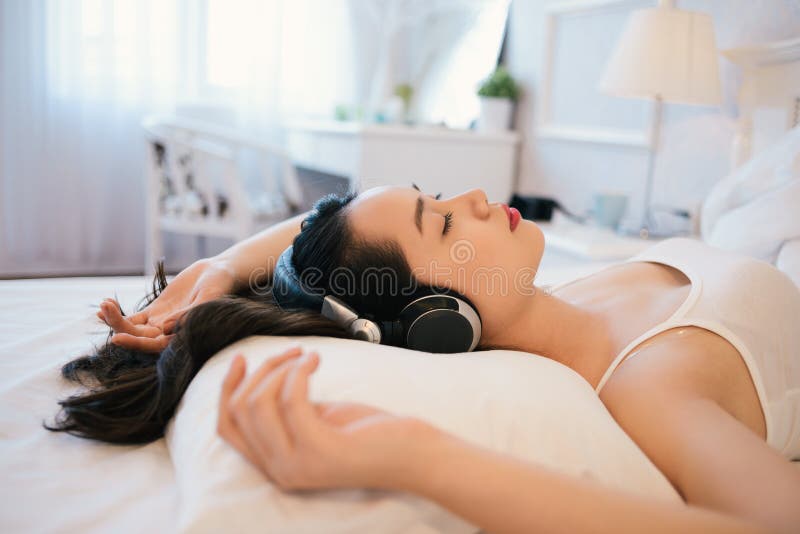 Young woman lying in bed and enjoying music with her eyes closed. Young woman lying in bed and enjoying music with her eyes closed