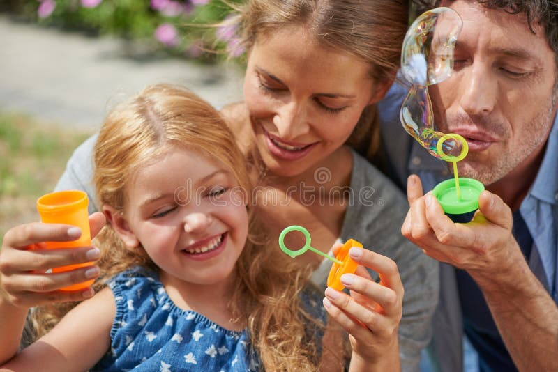 Genitori bambini e bolle nel giardino di casa, rilassati e giocherellati con un sorriso alla memoria. padre madre e immagine stock libera da diritti