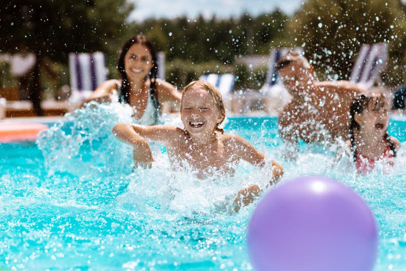 Genitori e bambini che ridono mentre giocando palla nella piscina fotografie stock libere da diritti Genitori e bambini che ridono mentre giocando palla nella piscina fotografie stock libere da diritti