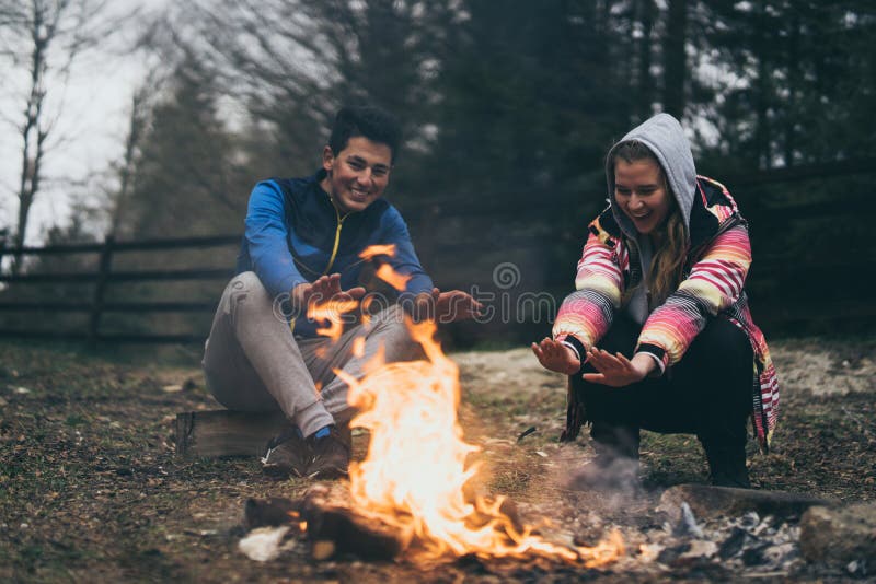Gente, concepto del turismo y de la naturaleza - tarde romántica, hombre y mujer que se sientan cerca de una hoguera foto de archivo Gente, concepto del turismo y de la naturaleza - tarde romántica, hombre y mujer que se sientan cerca de una hoguera foto de archivo