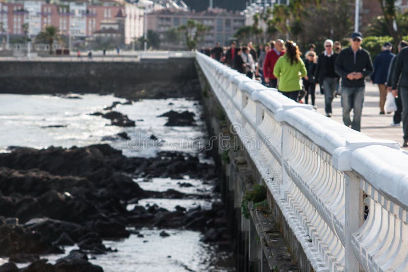 Gente Defocused che passeggiano lungo la passeggiata ed onde che si schiantano sulle rocce immagini stock Gente Defocused che passeggiano lungo la passeggiata ed onde che si schiantano sulle rocce immagini stock
