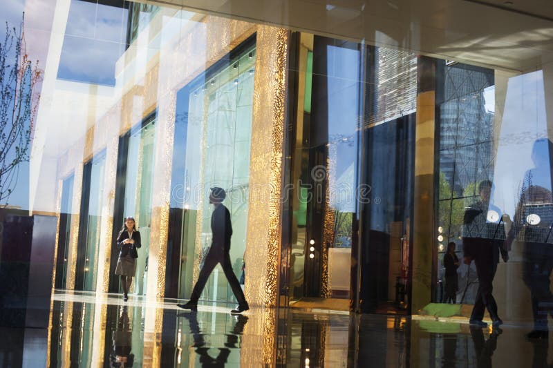 Gente di affari che cammina attraverso l'ingresso di un edificio per uffici dall'altro lato di una parete di vetro