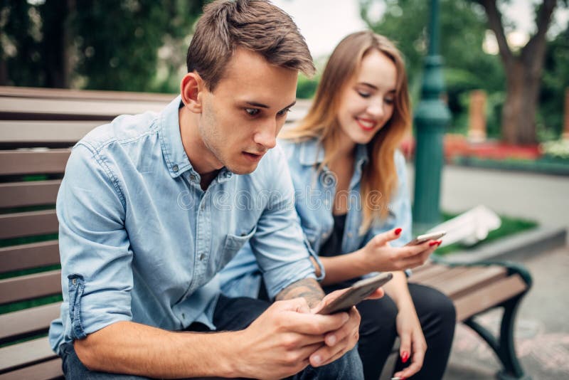 Phone addicted people, couple using their smartphones in summer park, social addict. Phone addicted people, couple using their smartphones in summer park, social addict