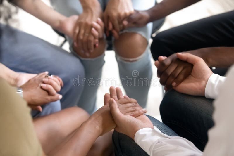 Gente diversa que se sienta en el círculo que lleva a cabo las manos en la terapia del grupo