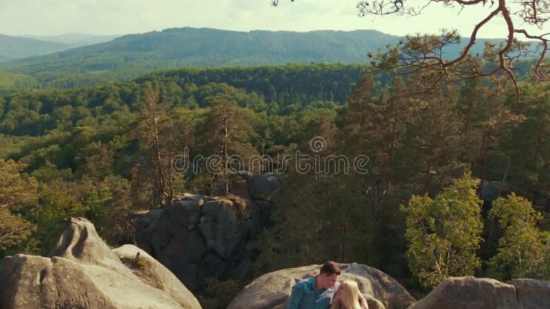 Gente joven apuesta en una ropa de sport Los amantes jovenes adorables están mintiendo en la piedra de la montaña rodeada por el