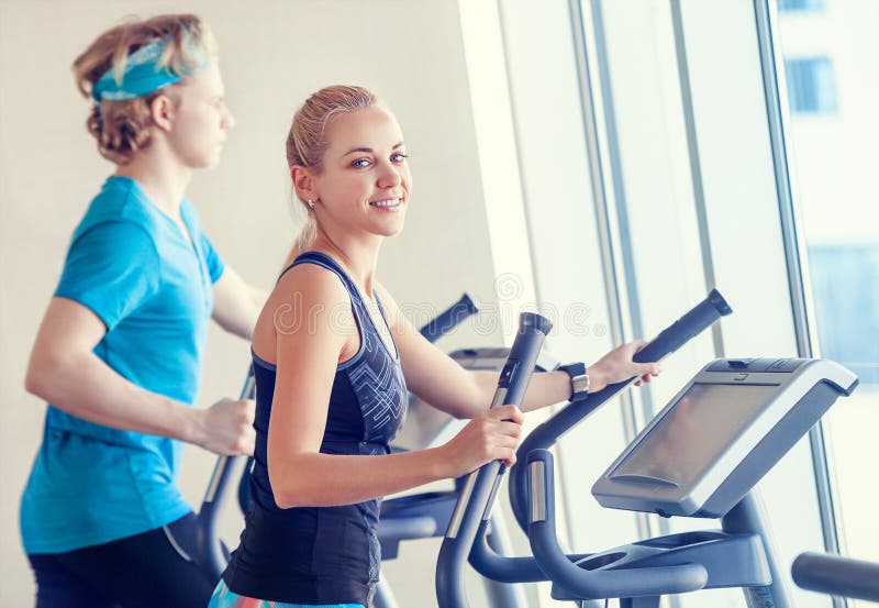 Gente joven en gimnasio moderno en el simulador del funcionamiento fotografía de archivo libre de regalías Gente joven en gimnasio moderno en el simulador del funcionamiento fotografía de archivo libre de regalías