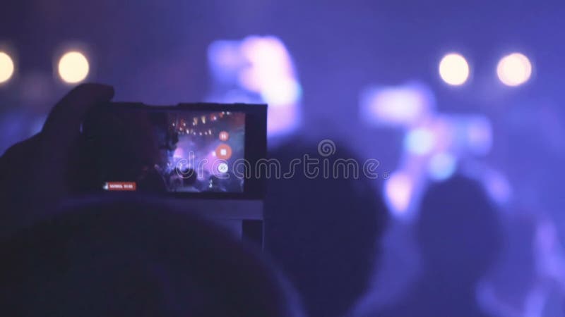 Gente que toma las fotos o que registra el vídeo con sus teléfonos elegantes en el concierto de la música