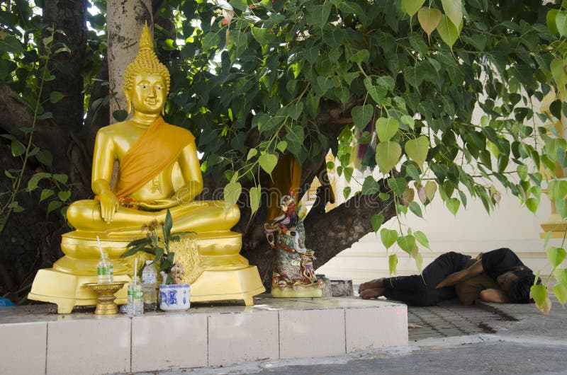 Gente tailandesa del vagabundo que duerme en piso debajo de religiosa de los ficus con la estatua de Buda foto de archivo Gente tailandesa del vagabundo que duerme en piso debajo de religiosa de los ficus con la estatua de Buda foto de archivo