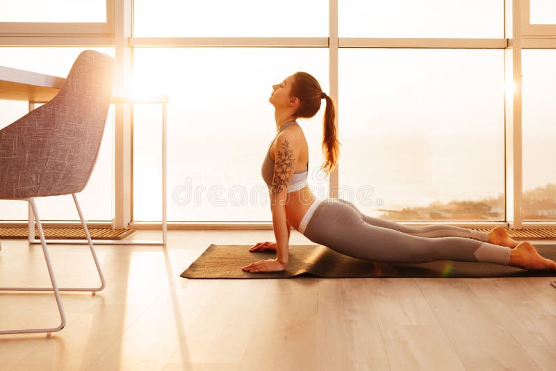 Gentille fille dans le dessus sportif et guêtres pratiquant le yoga sur le tapis de yoga à la maison au-dessus de la belle vue de photo stock Gentille fille dans le dessus sportif et guêtres pratiquant le yoga sur le tapis de yoga à la maison au-dessus de la belle vue de photo stock