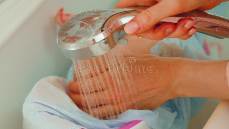 Mother washes a newborn baby with warm water in a tranquil bathroom atmosphere, focusing on the infants safety and