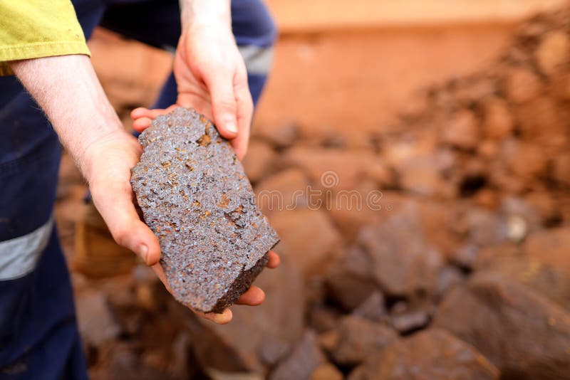 Geolog naukowy bada ręce nad poszukiwaniem skały z rudy żelaza na otwartym terenie kopalni