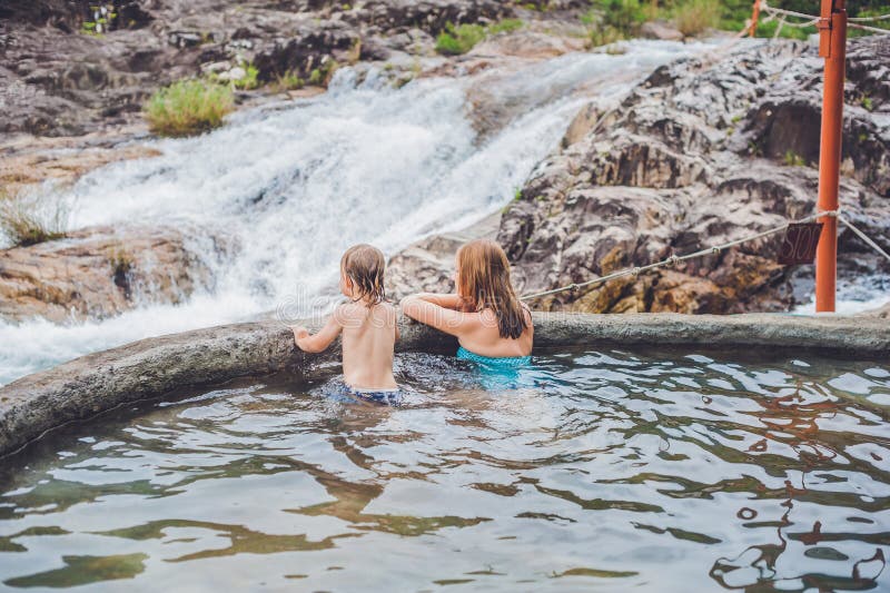 Geothermischer Badekurort Mutter und Sohn, die im Pool der heißen Quelle vor dem hintergrund eines Wasserfalls sich entspannen stockfotografie Geothermischer Badekurort Mutter und Sohn, die im Pool der heißen Quelle vor dem hintergrund eines Wasserfalls sich entspannen stockfotografie