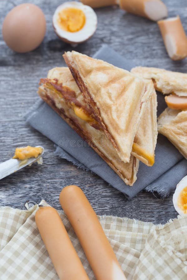 Gepresstes und geröstetes doppeltes panini mit dem Schinken und Käse gedient auf Sandwichpapier auf einem Holztisch, Ei, Würstche stockbild Gepresstes und geröstetes doppeltes panini mit dem Schinken und Käse gedient auf Sandwichpapier auf einem Holztisch, Ei, Würstche stockbild