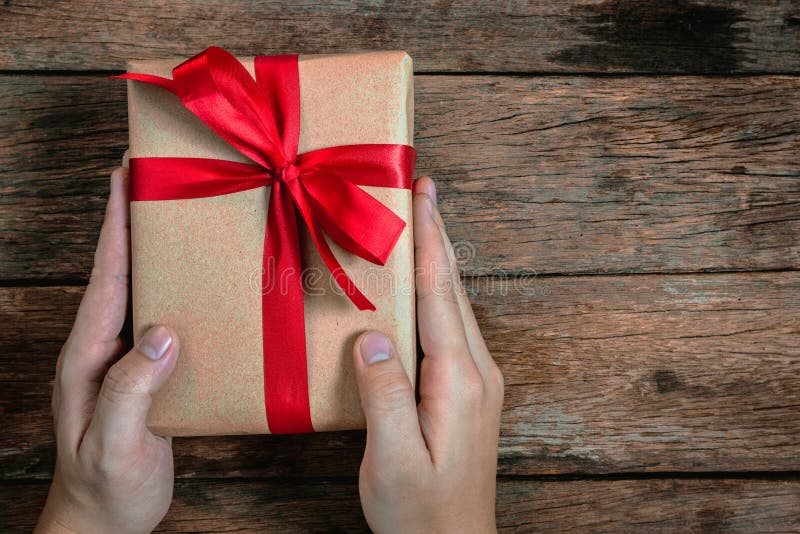 Ger den mänskliga manhanden för bonusen en närvarande brun fluga för gåvaask det röda bandet på gammal jul för bästa sikt för trä arkivbild Ger den mänskliga manhanden för bonusen en närvarande brun fluga för gåvaask det röda bandet på gammal jul för bästa sikt för trä arkivbild