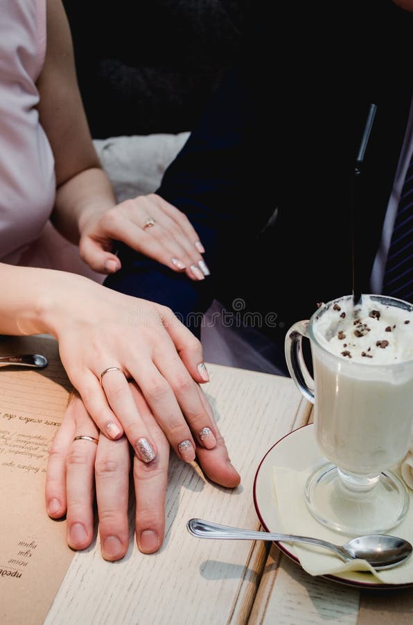 Gerade Griffhände des verheirateten Paars und Ehering im Café oben zeigen stockbild Gerade Griffhände des verheirateten Paars und Ehering im Café oben zeigen stockbild