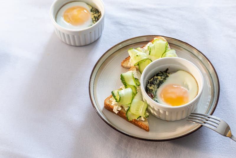 Shirred eggs Oeuf cocotte or baked eggs. healthy breakfast with eggs and spinach and toast with cucumber. Shirred eggs Oeuf cocotte or baked eggs. healthy breakfast with eggs and spinach and toast with cucumber.