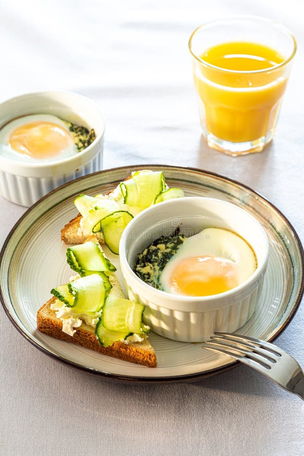 Shirred eggs Oeuf cocotte or baked eggs. healthy breakfast with eggs and spinach and toast with cucumber. Shirred eggs Oeuf cocotte or baked eggs. healthy breakfast with eggs and spinach and toast with cucumber.