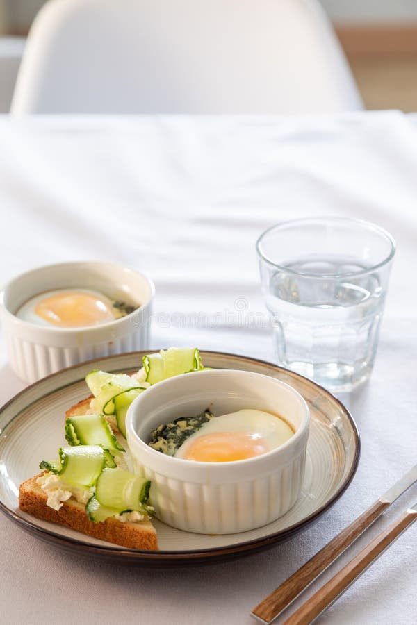 Shirred eggs Oeuf cocotte or baked eggs. healthy breakfast with eggs and spinach and toast with cucumber. Shirred eggs Oeuf cocotte or baked eggs. healthy breakfast with eggs and spinach and toast with cucumber.