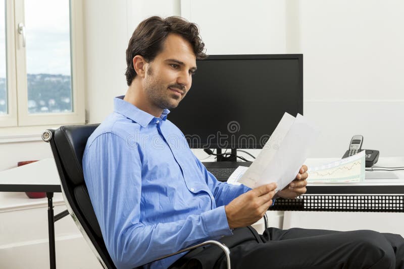 Gerente considerável novo que senta-se em sua mesa no escritório imagem de stock Gerente considerável novo que senta-se em sua mesa no escritório imagem de stock