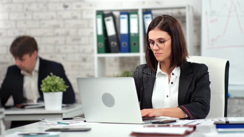 Gerichte, stijlvolle jonge zakenvrouw en man die op de moderne werkplek werkt en op het scherm van een laptop kijkt