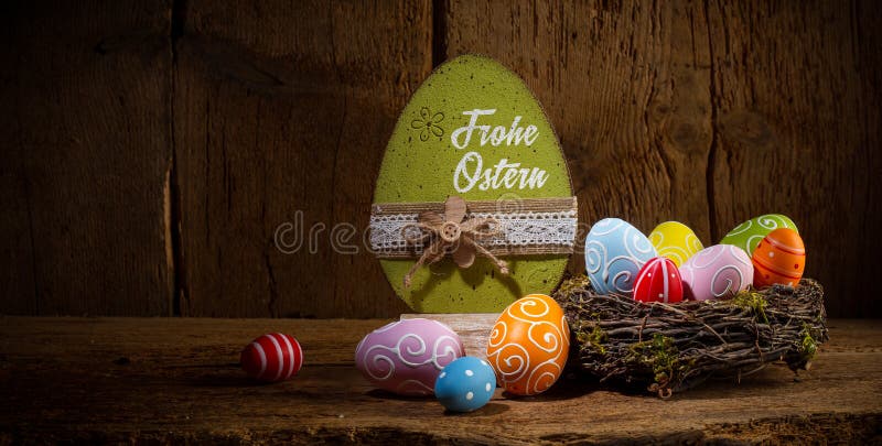 German greetings Frohe Ostern  english translation happy easter  Colorful painted eggs in birds nest basket on rustic wooden old