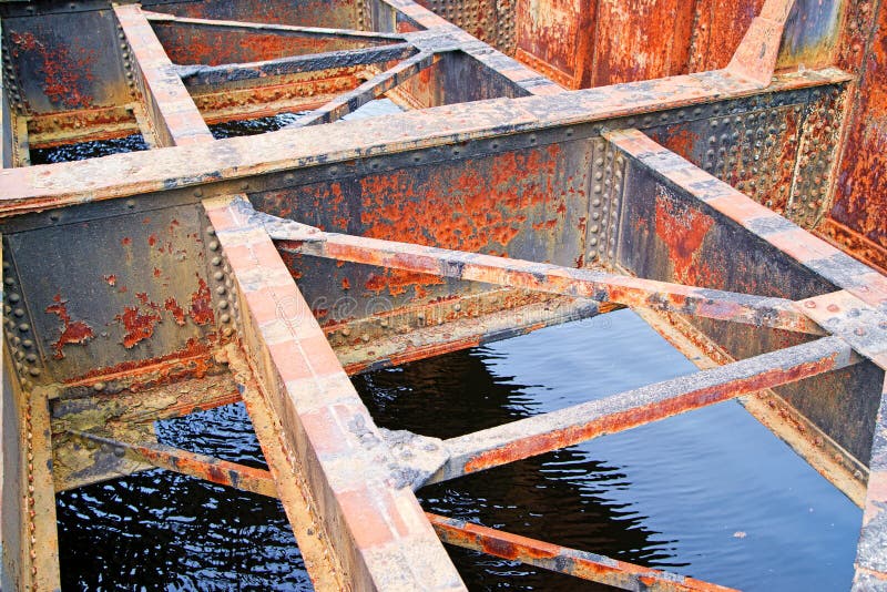 A grid work of beams that are worn and rusted over a body of water. A grid work of beams that are worn and rusted over a body of water.