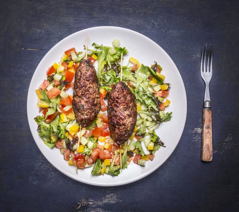 Geroosterde kebab op vleespen met een salade van diverse groenten op een witte plaat met een vork houten hoogste dicht mening rus stock foto Geroosterde kebab op vleespen met een salade van diverse groenten op een witte plaat met een vork houten hoogste dicht mening rus stock foto