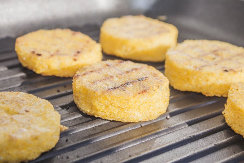 A grill pan full of yellow polenta cornmeal pucks. A grill pan full of yellow polenta cornmeal pucks