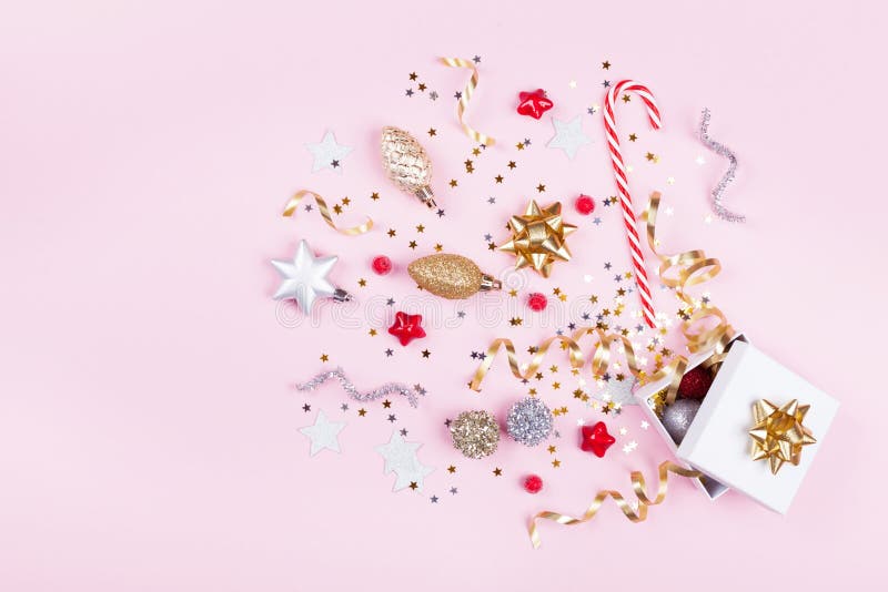 Geschenk oder Präsentkarton mit Konfettisternen, goldenem Band und Feiertagsdekoration auf rosa Pastellhintergrund Weihnachtseben