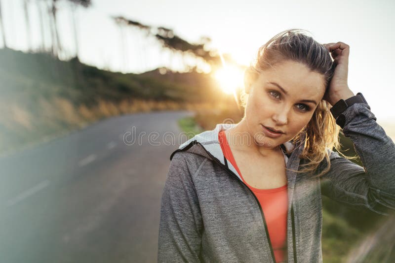Geschiktheidsvrouw die op straat met zon op de achtergrond lopen Portret van een vrouwelijke agent op een lege straat in de ochte stock fotografie Geschiktheidsvrouw die op straat met zon op de achtergrond lopen Portret van een vrouwelijke agent op een lege straat in de ochte stock fotografie