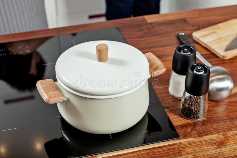 Geschlossene weiße Kasserolle mit hölzernen Stiften auf dem schwarzen Ofen und Glasgewürzmühlen mit papper und Salz auf der hölze lizenzfreies stockfoto Geschlossene weiße Kasserolle mit hölzernen Stiften auf dem schwarzen Ofen und Glasgewürzmühlen mit papper und Salz auf der hölze lizenzfreies stockfoto
