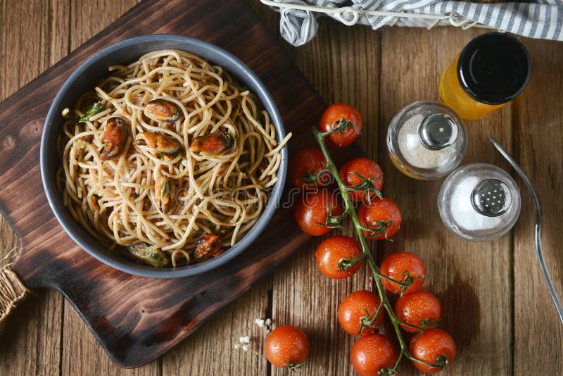 Geschmackvolle italienische Spaghettiteigwaren mit Miesmuschel, Tomate und Garnierung auf rundem Teller und hölzerner Platte für lizenzfreie stockfotos Geschmackvolle italienische Spaghettiteigwaren mit Miesmuschel, Tomate und Garnierung auf rundem Teller und hölzerner Platte für lizenzfreie stockfotos