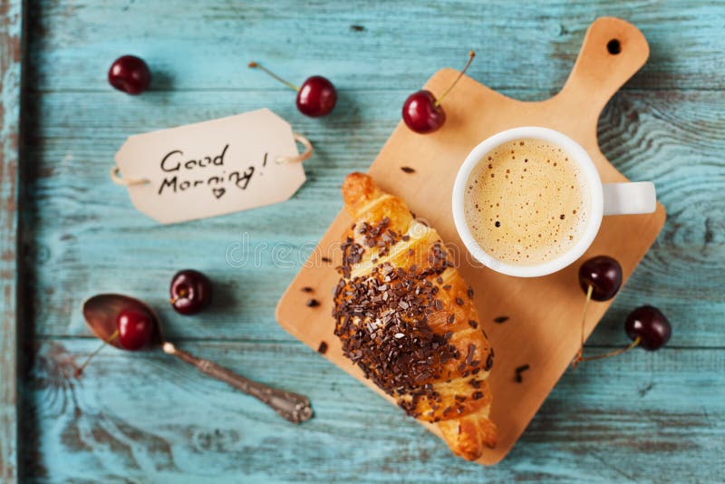 Geschmackvolles Frühstück mit neuem Hörnchen, Kaffee, Kirschen und Anmerkungen über einen Holztisch