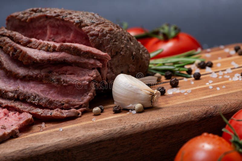 Geschnittenes bäuerisches saftiges Mais-Roastbeef geschmückt mit Tomaten, frischen Rosemary Herb-, Knoblauch-und Regenbogen-Pfeff lizenzfreie stockbilder Geschnittenes bäuerisches saftiges Mais-Roastbeef geschmückt mit Tomaten, frischen Rosemary Herb-, Knoblauch-und Regenbogen-Pfeff lizenzfreie stockbilder