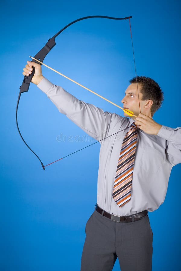 Young businessman holding bow and shooting to target. Blue background. Young businessman holding bow and shooting to target. Blue background