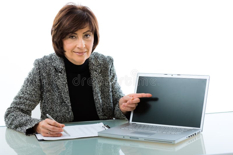 Senior businesswoman doing presentation, sitting at desk pointing at laptop screen (copy space). Senior businesswoman doing presentation, sitting at desk pointing at laptop screen (copy space).