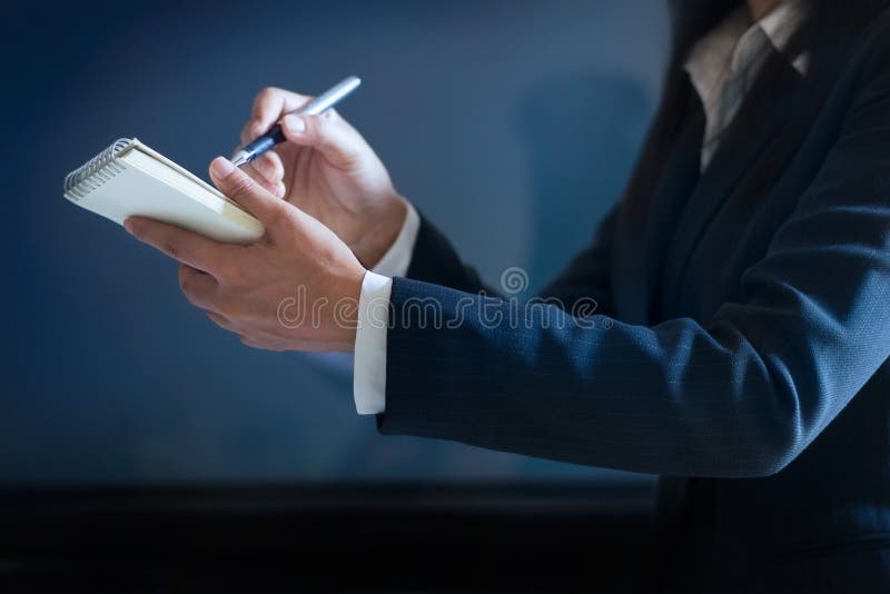 Geschäftsfrau, die Kenntnisse im Papier auf dunkelblauem Hintergrund nimmt lizenzfreie stockbilder Geschäftsfrau, die Kenntnisse im Papier auf dunkelblauem Hintergrund nimmt lizenzfreie stockbilder