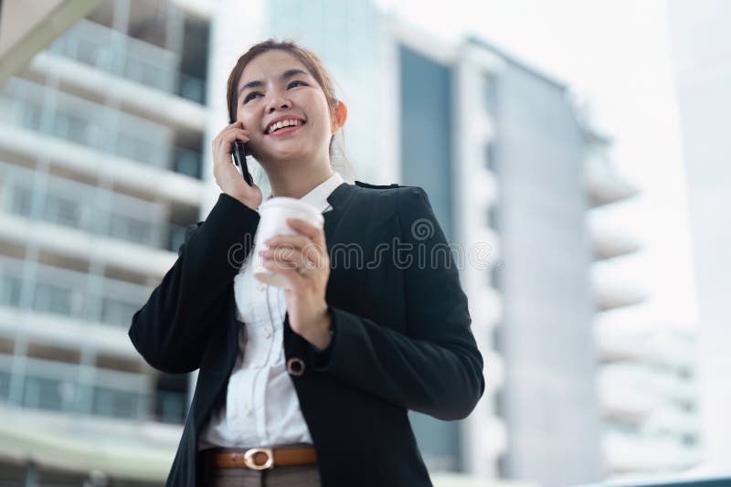Geschäftsfrau lächelt beim Telefonieren und hält Kaffeetasse im modernen urbanen Umfeld lizenzfreies stockfoto