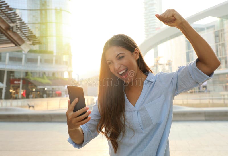 Geschäftsfrau startet den Tag mit guten Nachrichten auf ihrem Smartphone Glückliche Erfolgsfrau feiert im Freien jubelnd und hebt lizenzfreie stockfotos Geschäftsfrau startet den Tag mit guten Nachrichten auf ihrem Smartphone Glückliche Erfolgsfrau feiert im Freien jubelnd und hebt lizenzfreie stockfotos