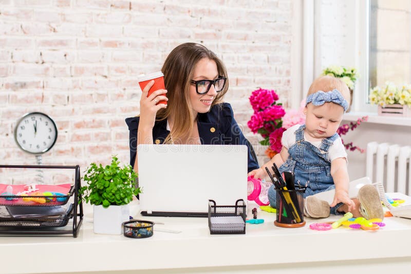 Geschäftsfraumutterfrau mit einer Tochter, die am Computer arbeitet. Geschäftsfraumutterfrauen mit einer Tochter, die am Computer arbeitet Am Arbeitsplatz zusammen mit einem kleinen Kind