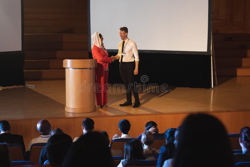 Geschäftskollegestellung und Diskussion mit einander vor dem Publikum im Auditorium lizenzfreie stockbilder Geschäftskollegestellung und Diskussion mit einander vor dem Publikum im Auditorium lizenzfreie stockbilder