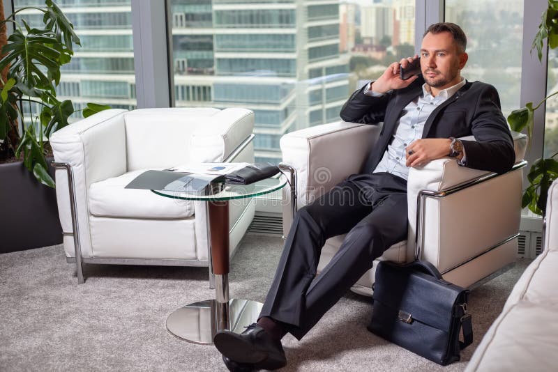 Geschäftsmann in der Klage sprechend am Handy, der in einem Sessel sitzt lizenzfreie stockfotos Geschäftsmann in der Klage sprechend am Handy, der in einem Sessel sitzt lizenzfreie stockfotos